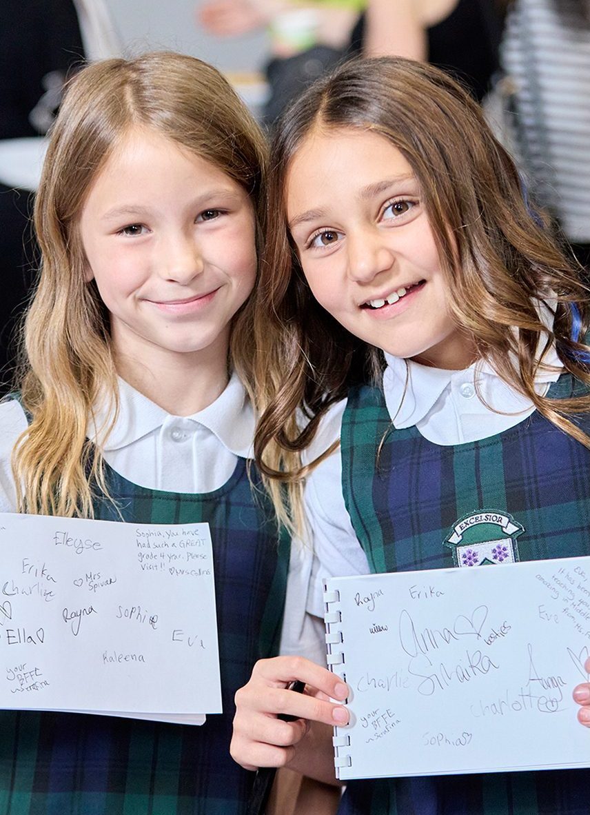 two girl students holding up papers